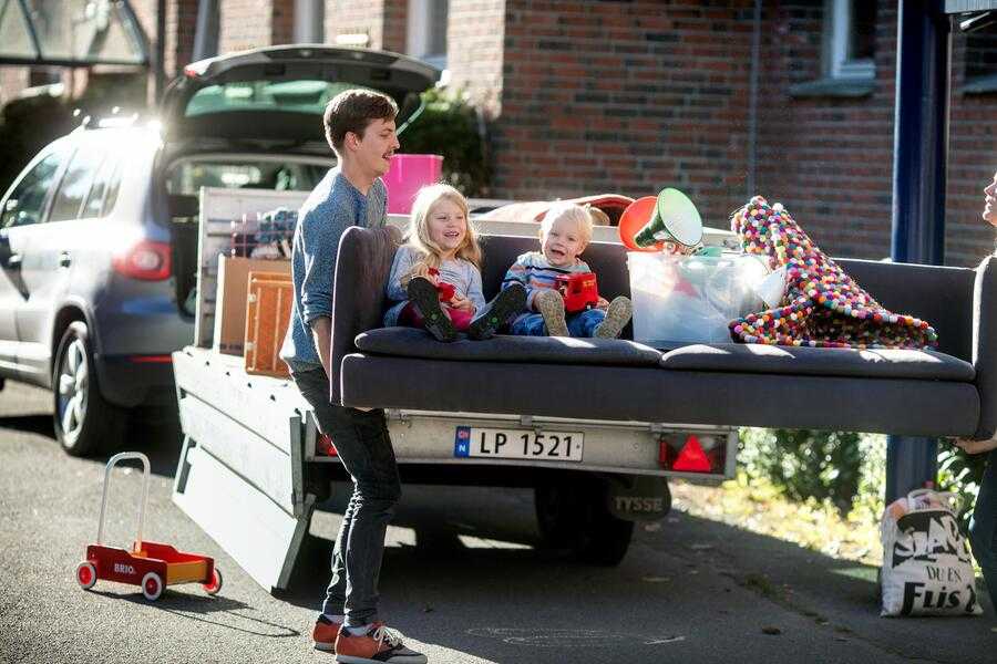 Et par bærer en sofa med to barn i fra en bilhenger.