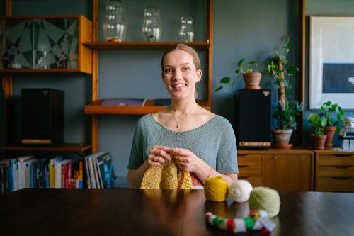Ung kvinne som smiler og strikker, sittende ved et bord med garnnøster.