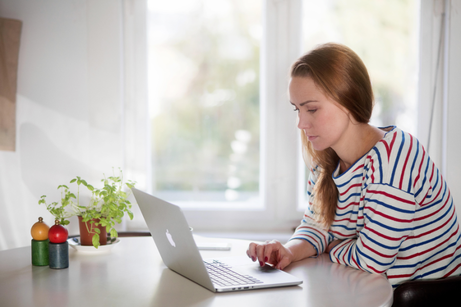 Kvinne med langt hår sitter foran en datamaskin hjemme