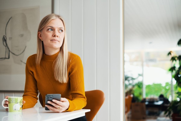 Kvinne sittende ved bord med mobil i hånden