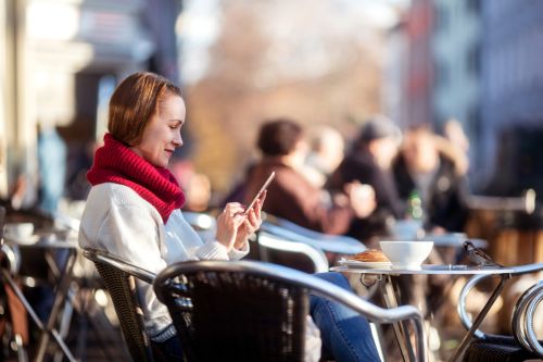 Kvinne på utekafe ser på mobilen sin