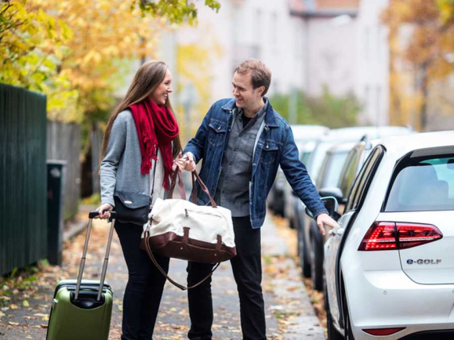 Et smilende par med en bag og en trillekoffert utenfor en bil