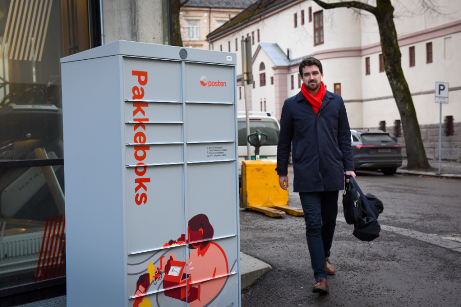 Man with bags approaching a Pakkeboks (parcellocker) in urban area