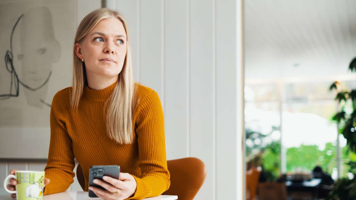 Kvinne sittende ved bord med mobil i hånden