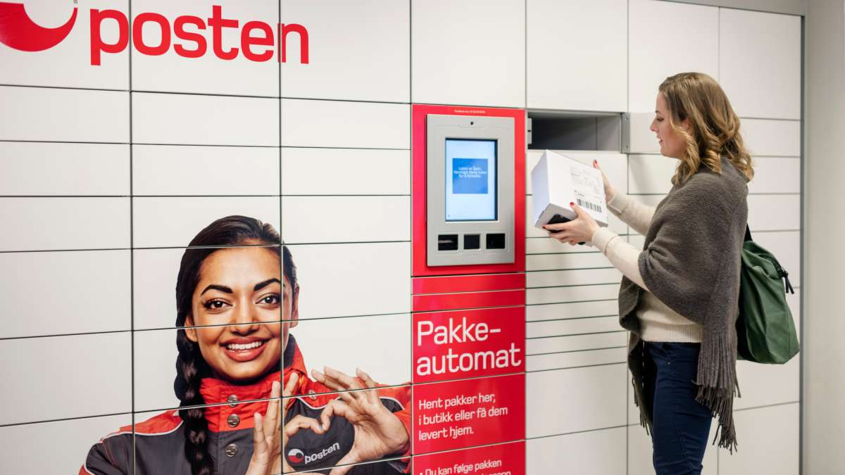 Kvinne med en pakke i hendene som står foran en pakkeautomat