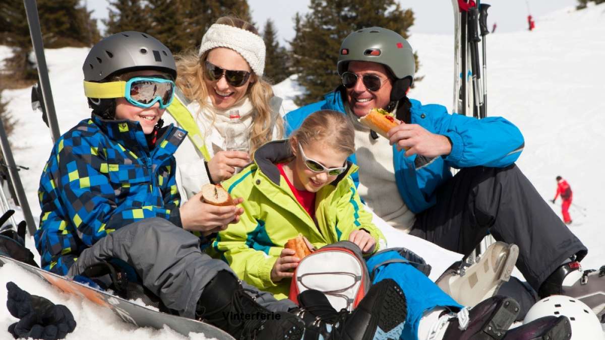 Glad familie på skitur, sitter ned og spiser matpakke