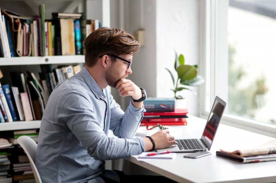 Mann sitter ved et bord foran en laptop.