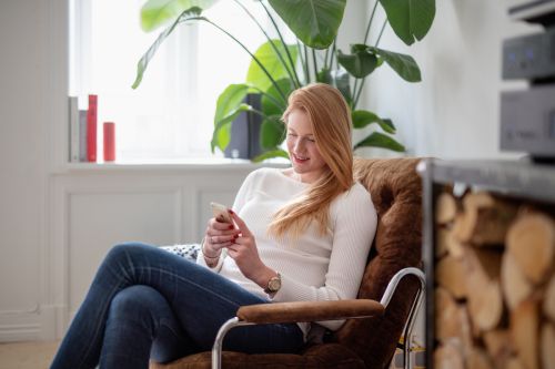 Kvinne sitter i lenestol og ser på mobilen sin