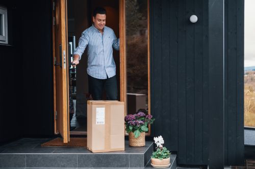 Mann åpner inngangsdøra og ser at det er levert en pakke til ham